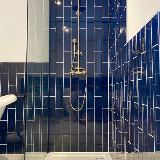 Gold shower mounted on blue tiles.