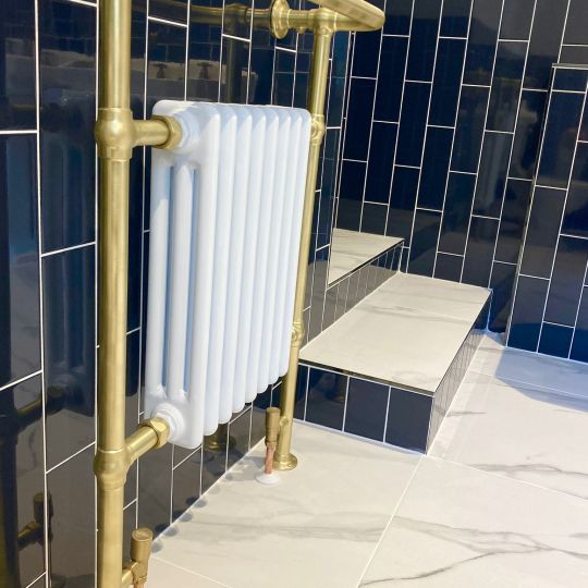White radiator with gold pipe-work. Blue brickwork style tiles, mounted vertically