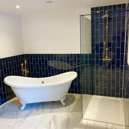Free-standing bath with gold taps. Blue bathroom tiles