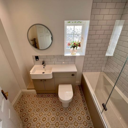 Bathroom unit comprising sink and toilet plus worktop area. Shower over bath. White/Grey wall tiles in brickwork pattern