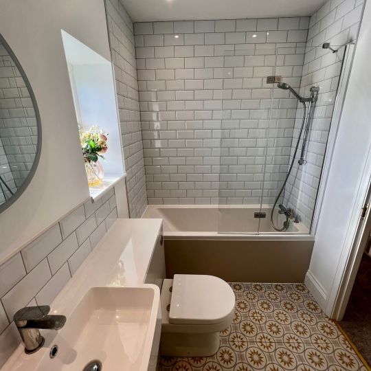 Mosaic tiled bathroom floor with grey-white tiled walls. Piha Plumbing and Bathroom Installations