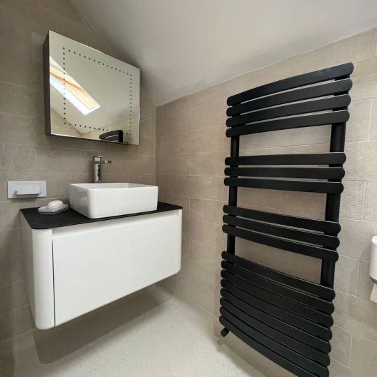 Black wall-mounted towel rail. White and black wall-mounted sink and storage. Piha Plumbing and Bathroom Installations